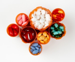 several prescription bottles filled with colorfu pills and capsules, shot from above on white background with soft white drop shadow